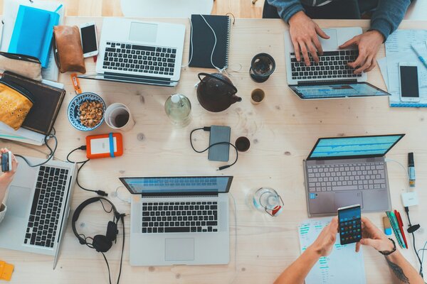 View down on a table with several people working on their laptops, mobile, peanuts, cables, etc. Photo by Marvin Meyer on Unsplash