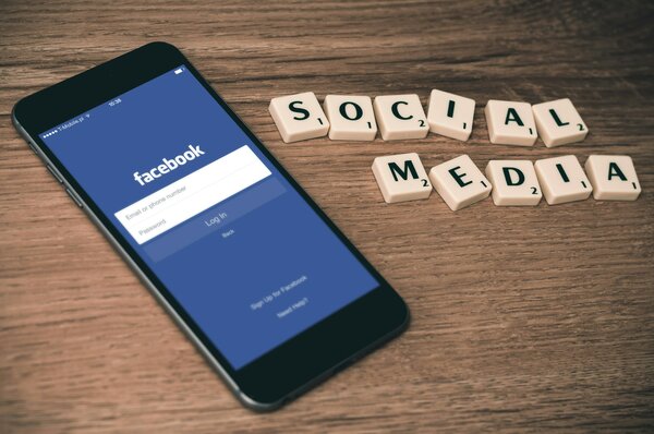 Mobile screen with a login page for Facebook. "Social media" spelled with Scrabble pieces.Photo by Firmbee.com on Unsplash.