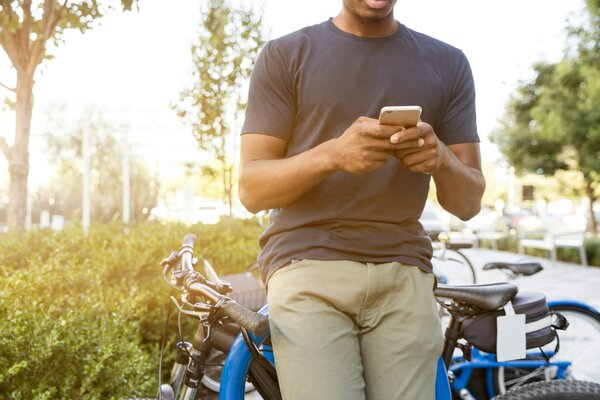 Young man leaning on his bike in the street and looking at his phone. Bright background with bushes and tress bathed in light and a row of bikes behind the main person. Photo by Linkedin sales solutions on Unsplash