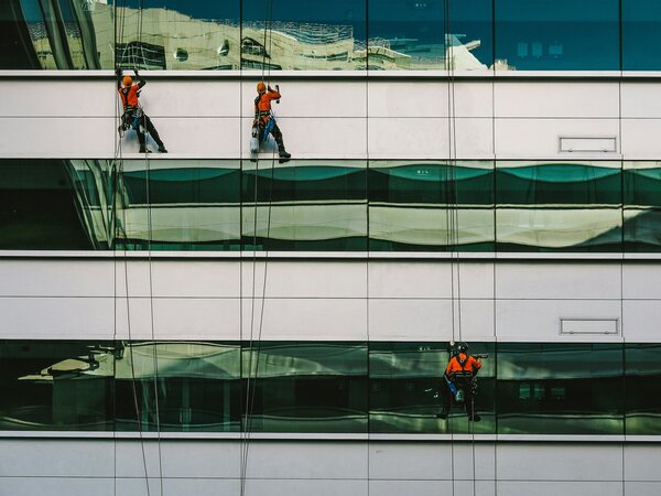 Window cleaners in Lisboa, Portugal. Three men hanging down the side of a building with three horizontal lines of windows. Photo by Nuno Silva on Unsplash.